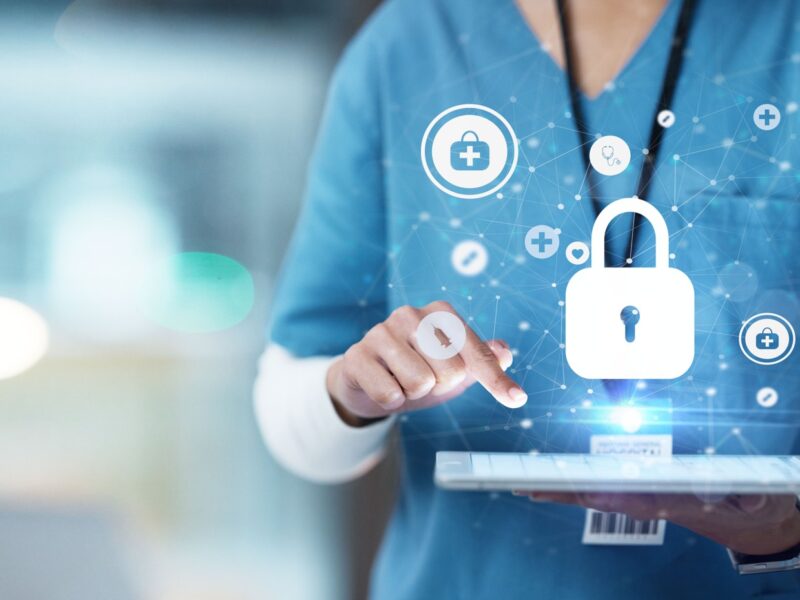 A medical practitioner is holding a tablet face-up. Security icons are hovering over the screen.