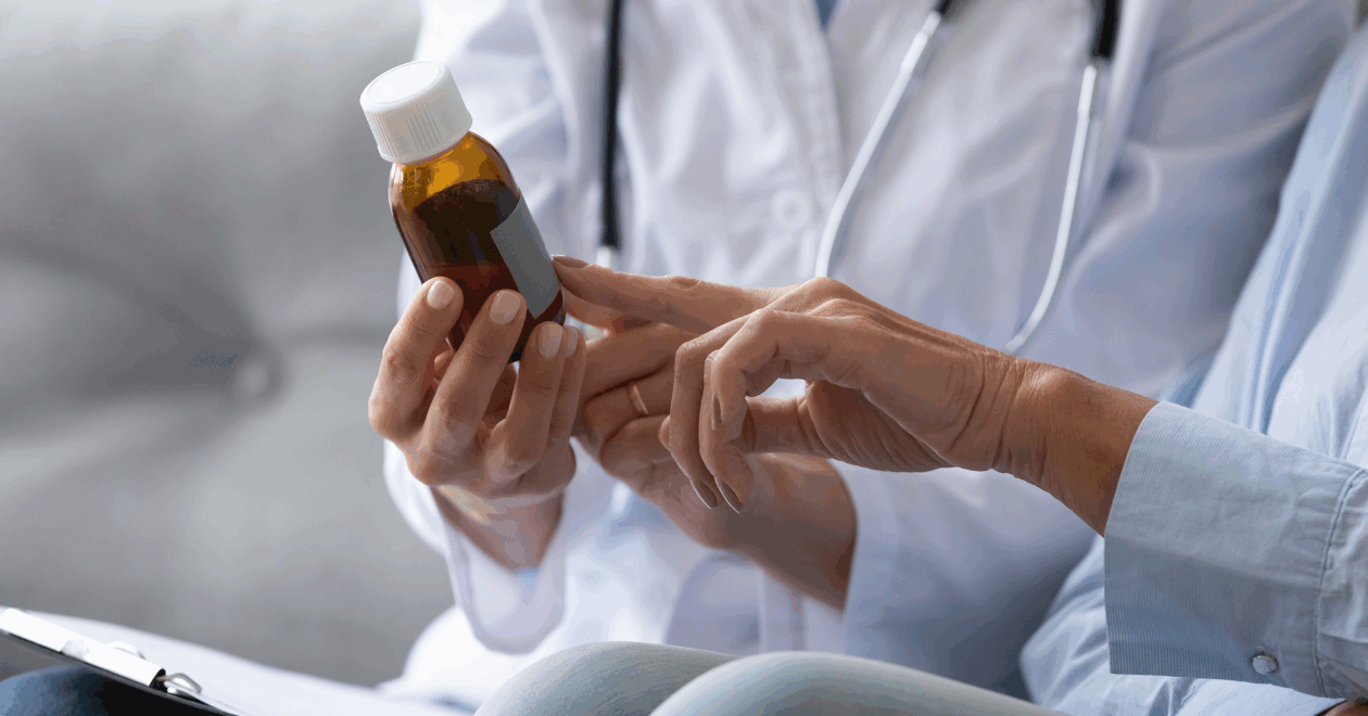 Close up of a female doctor's hands as she holds up a prescription bottle and shows it to a female patient.