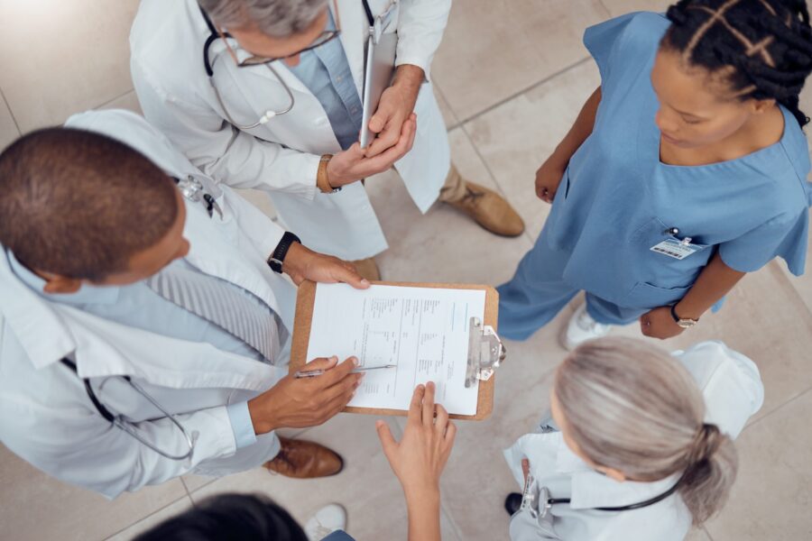 Overhead view of several healthcare professionals standing together and reviewing a clipboard with printed documents in a clinical setting.
