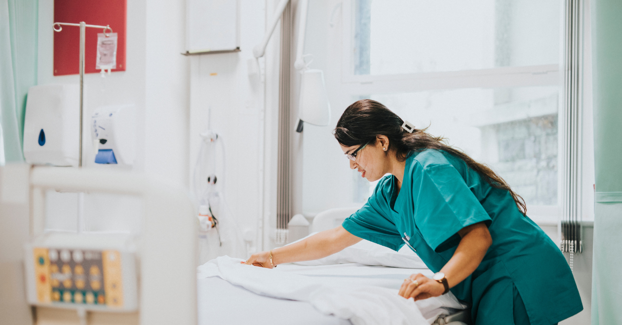 A healthcare worker making a bed in a clinical room, overlaid with the Hub's graphic device - curved colour bands and the title: Case Study – Strengthening linen and laundry services across the East of England through procurements worth over £100 million.