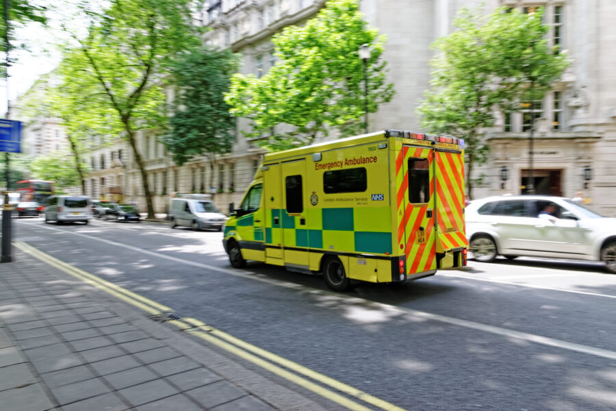 An ambulance is driving down a road with leafy green trees lining the sides.