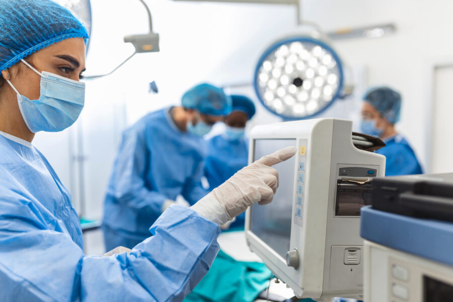 A female surgeon is in theatre pointing at a monitor whilst other surgeons are in the background